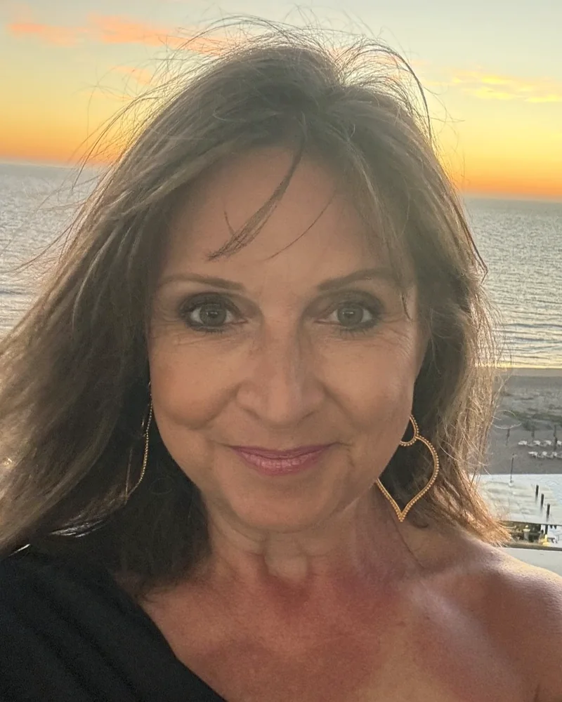Paula Fehringer, esthetician and owner of Ever Grace Skin Studio, smiling in a portrait taken at sunset by the ocean